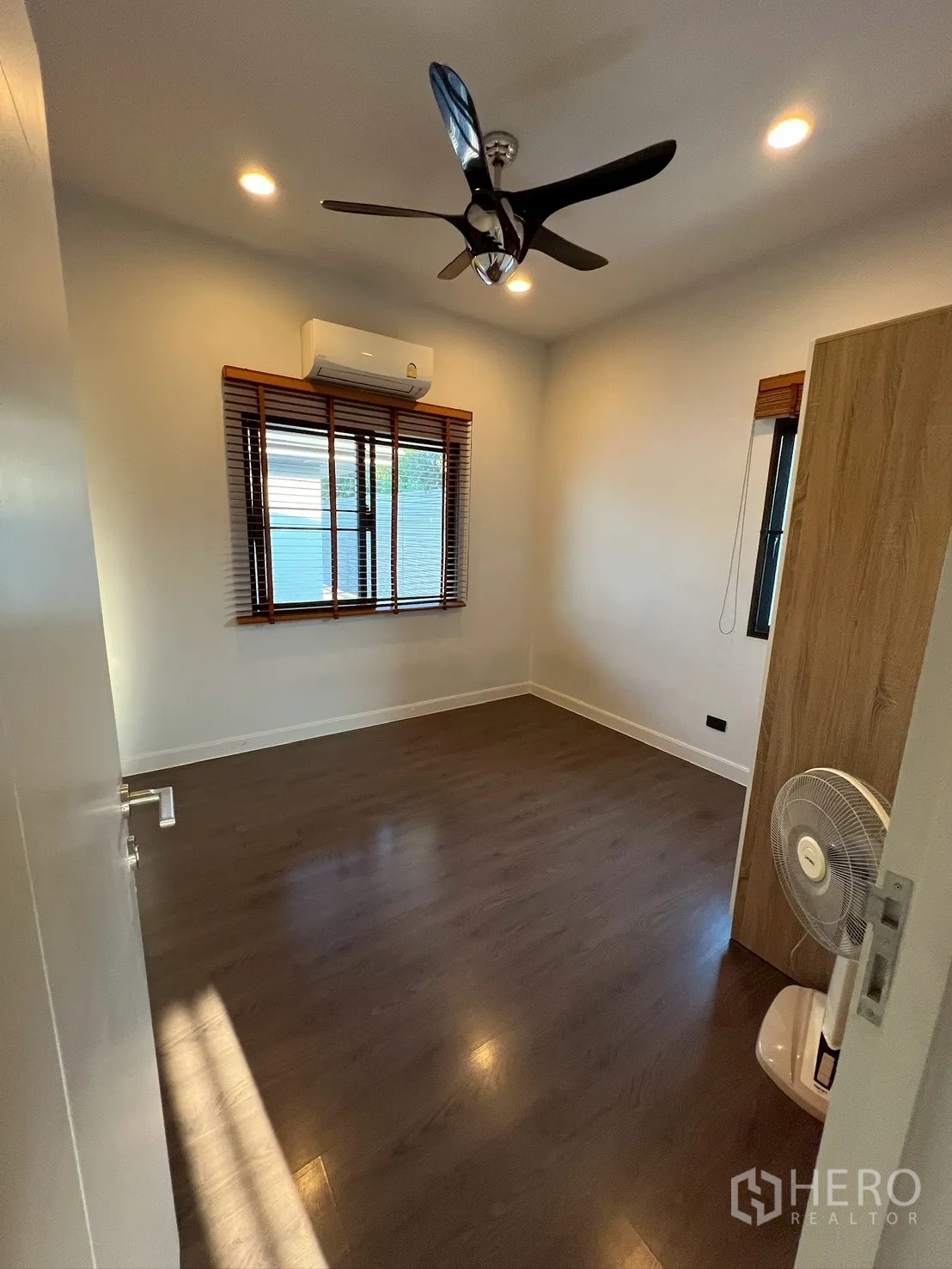Detached House for rent in Bang Kapi, Bangkok - Cozy bedroom with air conditioner, ceiling fan, and two windows with wooden blinds.