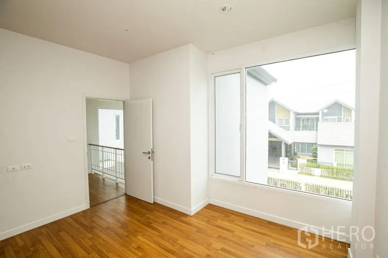 Detached House for rent or sale in Lam Luk Ka, Pathum Thani - Bright corridor with windows and wood flooring connecting bedrooms.