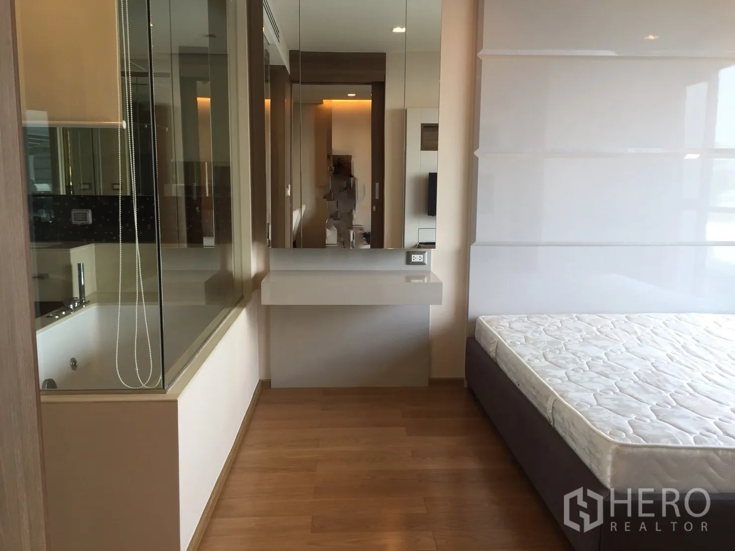 公寓 出租在Bang Rak, Bangkok - 明亮卧室，木地板与梳妆台，通过玻璃隔断与带浸泡浴缸的浴室相连。