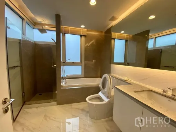 Condominium for rent in Khlong Luang, Pathum Thani - Modern bathroom featuring a bathtub, glass shower, large mirror and marble surfaces.
