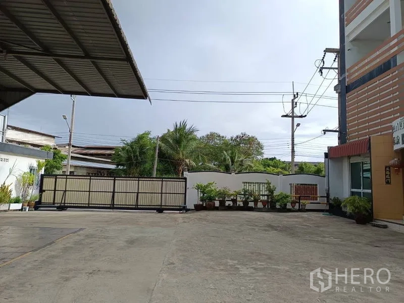 โรงงาน ขายในBan Phaeo, Samut Sakhon - ประตูรั้วเลื่อนพร้อมลานคอนกรีตกว้าง สายไฟเหนือศีรษะและต้นไม้รอบด้าน