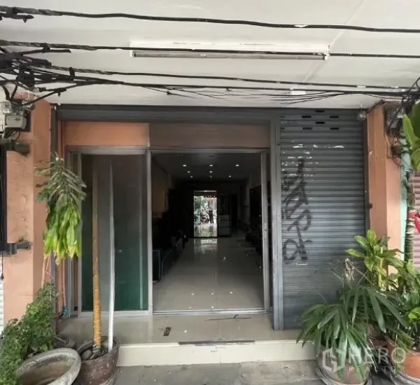 Shophouse for rent in Phra Khanong, Bangkok - Shophouse entrance with partially open roller shutter and glass door.