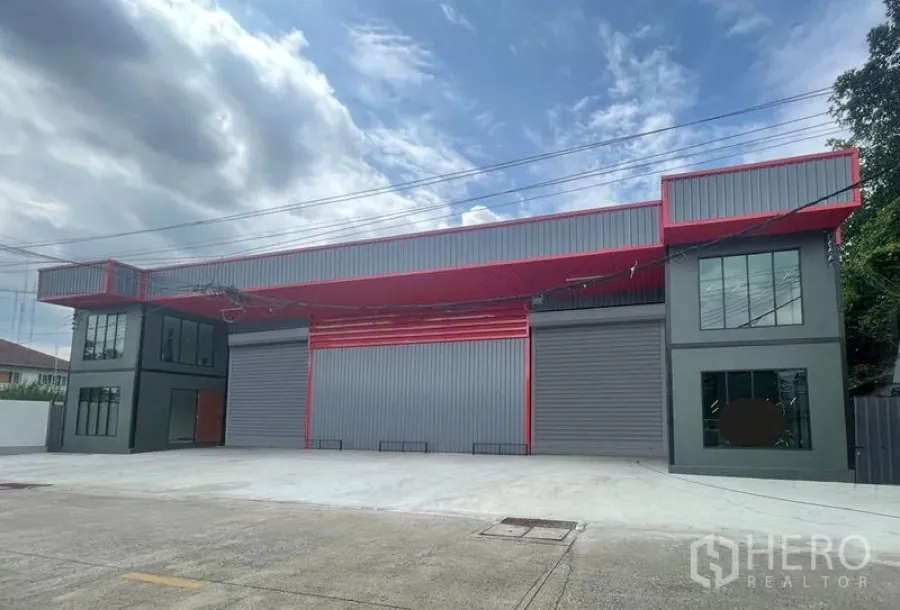 Warehouse for rent or sale in Lam Luk Ka, Pathum Thani - Modern grey and red warehouse exterior in Lam Luk Ka, Pathum Thani with twin large roller shutters, two-storey office wings and a wide concrete forecourt.