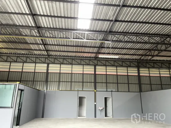 Factory for rent in Khlong Luang, Pathum Thani - High ceiling with steel beams and translucent panels above two restroom doors and a wall-mounted sink.