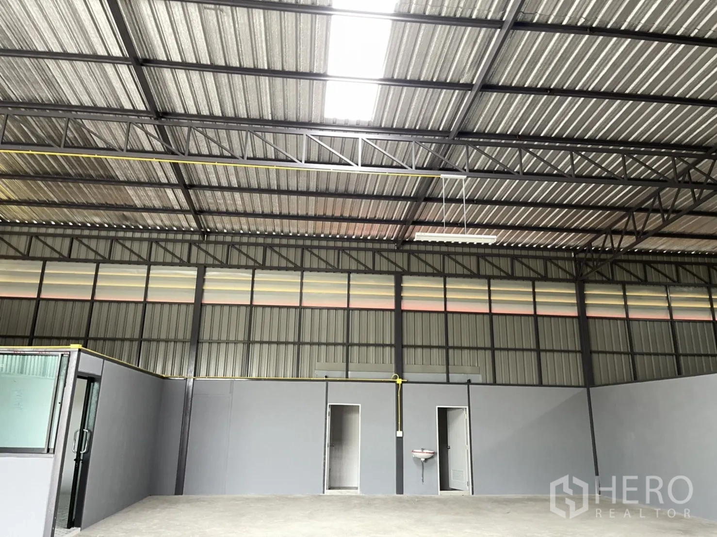 Factory for rent in Khlong Luang, Pathum Thani - High ceiling with steel beams and translucent panels above two restroom doors and a wall-mounted sink.