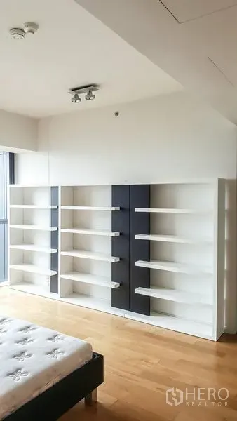 Condominium for rent or sale in Sathon, Bangkok - Bedroom corner with built-in white shelving units and wood flooring near a large window.