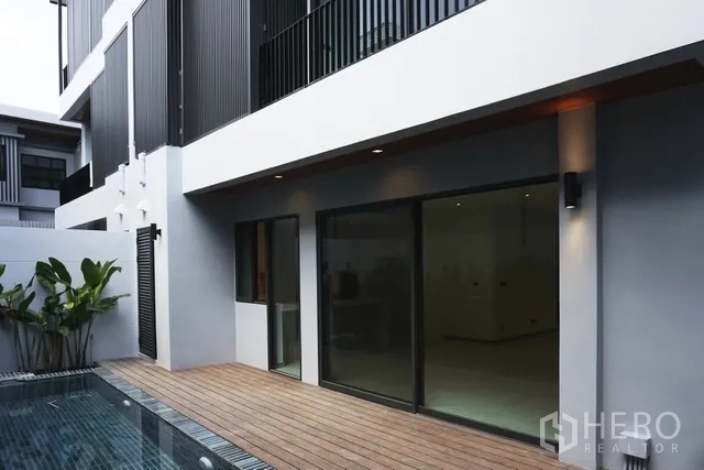 独栋房屋 for rent in Watthana, Bangkok - 泳池旁木平台，推拉玻璃门通向室内。