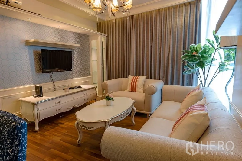 คอนโด ให้เช่าในWatthana, Bangkok - ห้องนั่งเล่นโซฟาครีม โต๊ะกลาง ชั้นวางทีวี โคมระย้า หน้าต่างสูงและต้นไม้ในห้อง