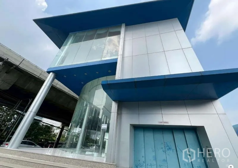 Showroom for rent - Curved glass entrance with silver cladding and blue canopy at the showroom facade.