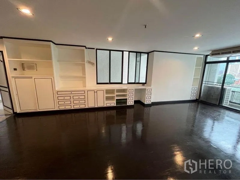 Condominium for rent or sale in Watthana, Bangkok - Spacious living room with full built-in shelving and sliding door to balcony.