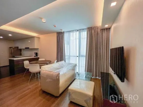 คอนโด ขายในHuai Khwang, Bangkok - โซนนั่งเล่นพร้อมชุดโซฟา ทีวี ผ้าม่านสูงจรดเพดาน และโต๊ะทานข้าวข้างครัว