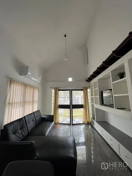 Detached House for rent in Saphan Sung, Bangkok - High-ceiling living room with black leather sofa, built-in media wall and sliding glass doors.