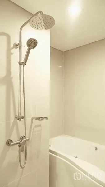 Condominium for rent in Watthana, Bangkok - Modern bathroom with rain shower and bathtub finished in light tiles.