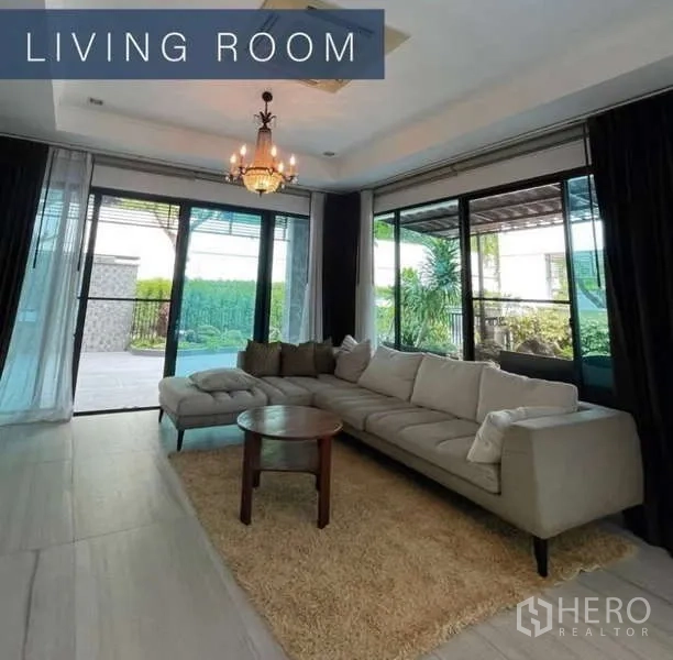 Detached House for sale in Khlong Toei, Bangkok - Living room with L-shaped sofa, chandelier and sliding glass doors to the patio.