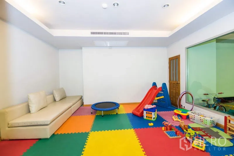 Apartment for rent in Sathon, Bangkok - Indoor children’s playroom with colorful mats, slide, toys and sofa seating.