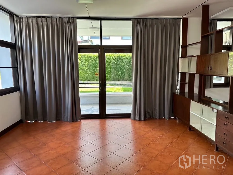 Detached House for rent in Phra Khanong, Bangkok - Bright living room with terracotta floor, full-height glass doors, curtains and built-in shelving.
