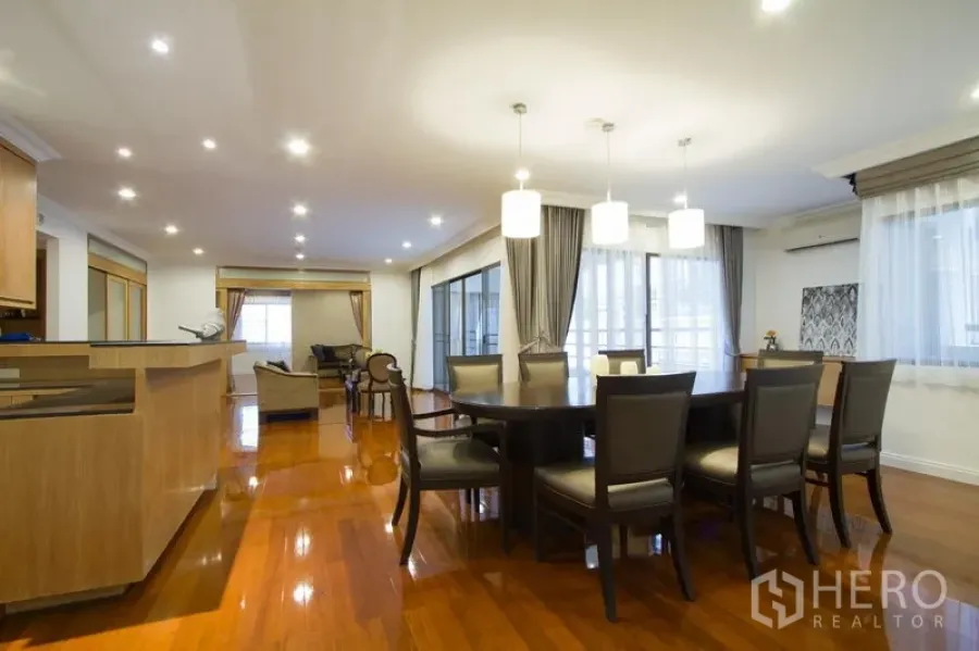 Apartment for rent in Watthana, Bangkok - Open-plan dining and living area with pendant lights, round table, and glossy hardwood floors by large windows.