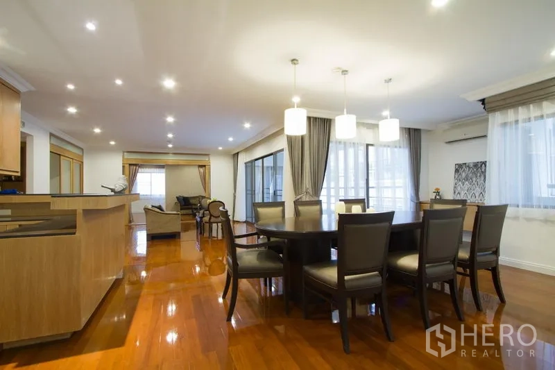 Apartment for rent in Watthana, Bangkok - Open-plan dining and living area with pendant lights, round table, and glossy hardwood floors by large windows.
