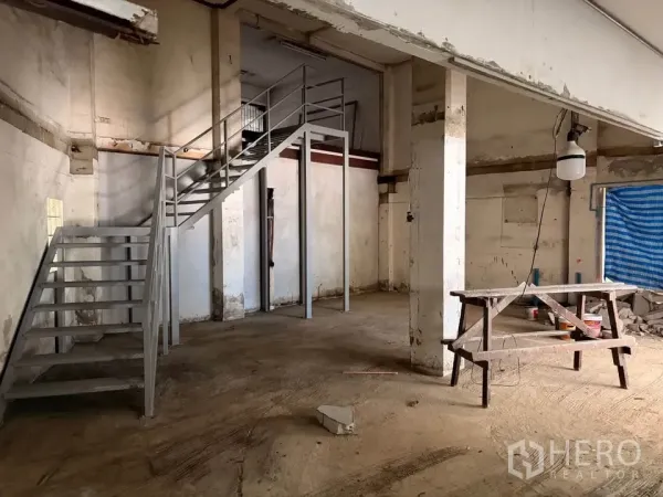 Retail Space for rent in Watthana, Bangkok - Unfinished space with a metal staircase leading to a mezzanine, concrete columns, and a workbench.