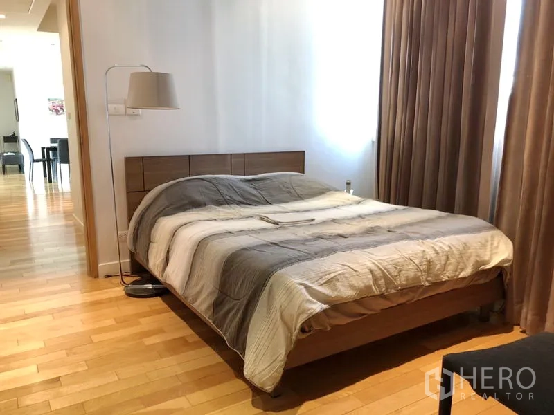 Condominium for rent in Khlong Toei, Bangkok - Bedroom with king-size bed, floor lamp, full-length curtains and wood flooring.