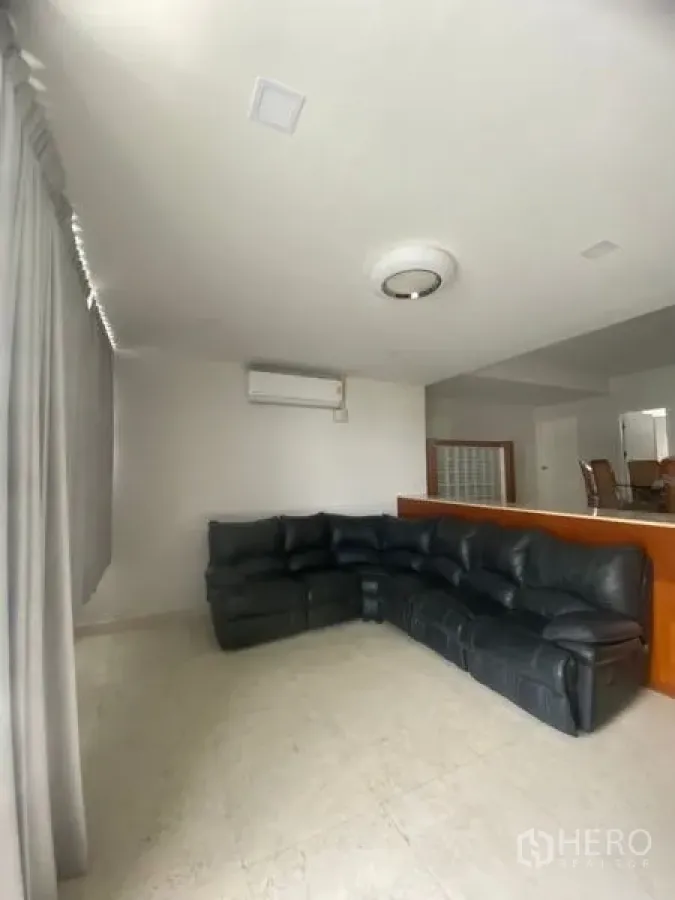 Condominium for rent in Sathon, Bangkok - Bright living room with a large black leather sectional sofa, tiled floor, air conditioning, and full-length curtains.