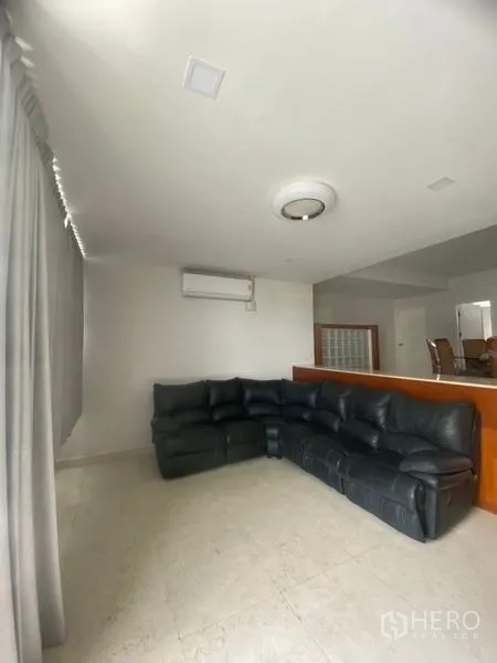 Condominium for rent in Sathon, Bangkok - Bright living room with a large black leather sectional sofa, tiled floor, air conditioning, and full-length curtains.