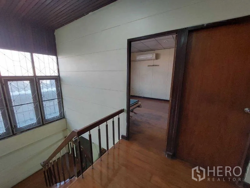 Townhouse for sale - Upper landing with wooden stairs, tall window, and a doorway leading to an air-conditioned bedroom.