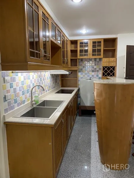 Condominium for rent or sale in Watthana, Bangkok - Galley kitchen with wooden cabinets, double sink, stone countertops, colorful mosaic backsplash and a built-in wine rack.