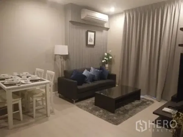 คอนโด ให้เช่าในHuai Khwang, Bangkok - ห้องนั่งเล่นอบอุ่นพร้อมโซฟาสีเทา โต๊ะกลาง พรม และมุมรับประทานอาหารใต้แสงไฟนุ่ม