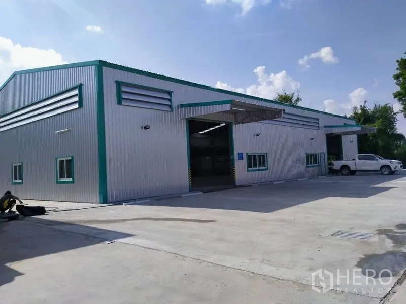 货栈 出租在Mueang Nonthaburi, Nonthaburi - 暖色金属外墙仓库外观，宽阔混凝土场地与装卸雨棚，位于暖武里直辖县。