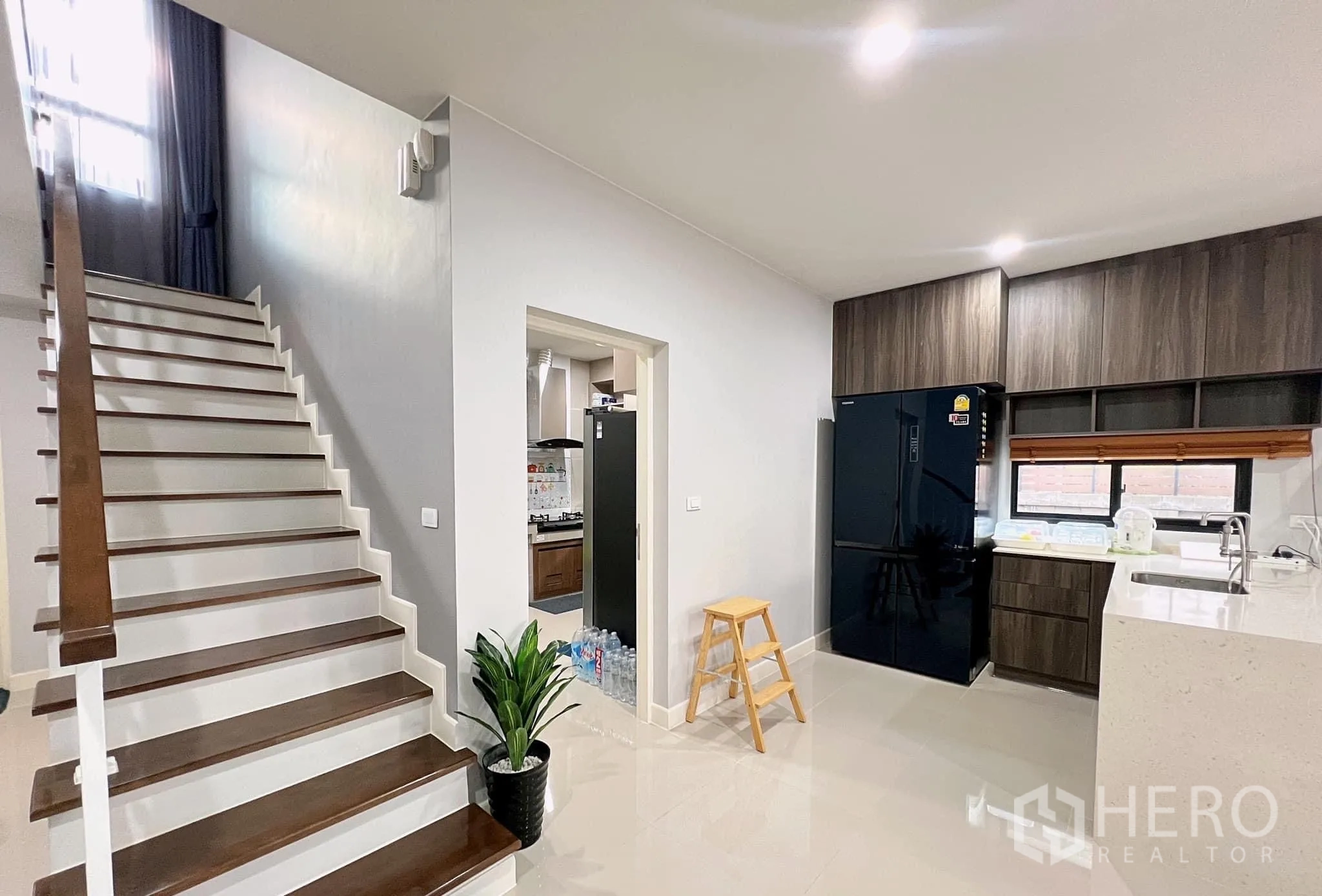 Detached House for rent or sale in Lam Luk Ka, Pathum Thani - Ground floor stairway beside open kitchen with island and tall fridge.