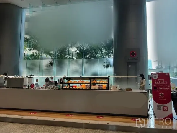 零售空间 出租在Bang Rak, Bangkok - CBD 大堂中的现代零售柜台，带发光展示柜与高大圆柱及大片磨砂玻璃背景。