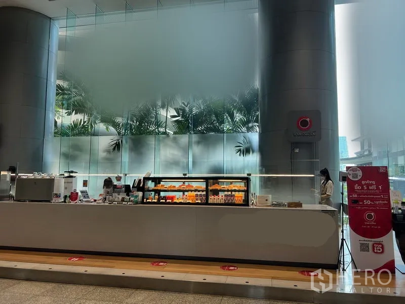 零售空间 出租在Bang Rak, Bangkok - CBD 大堂中的现代零售柜台，带发光展示柜与高大圆柱及大片磨砂玻璃背景。