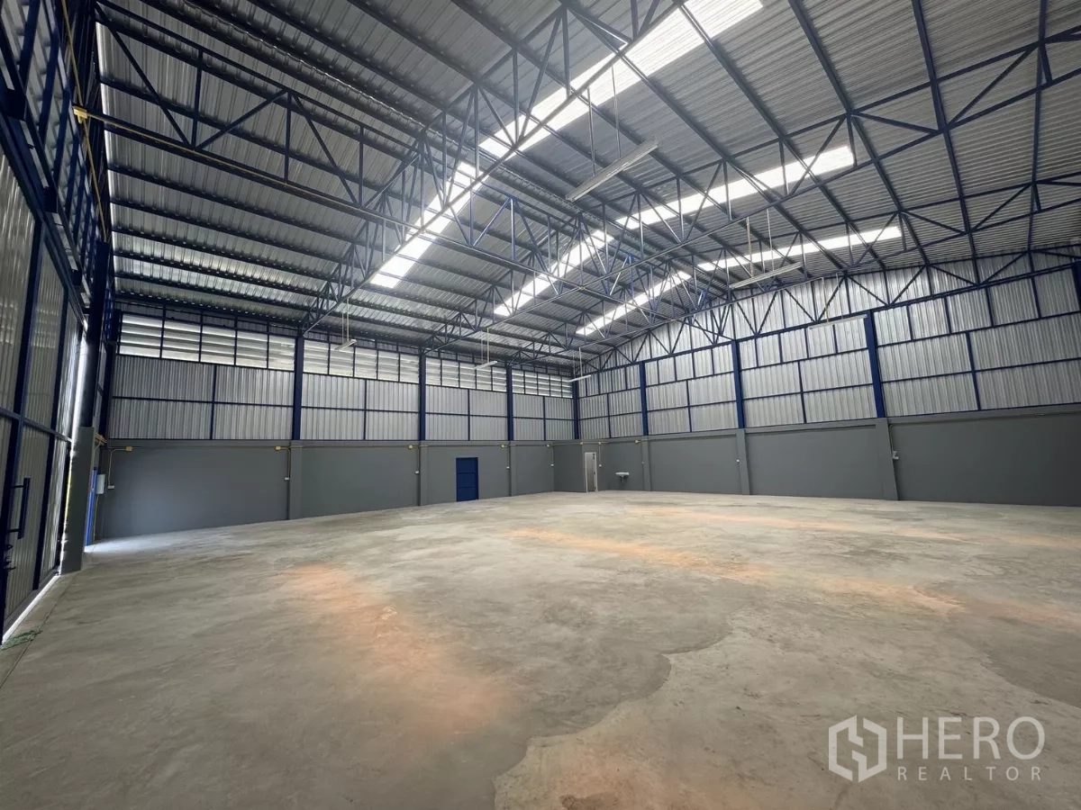 Warehouse for rent in Bang Phli, Samut Prakan - Spacious empty warehouse interior with high steel truss roof, skylight panels, concrete floor and multiple exit doors.