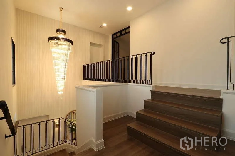 Detached House for rent in Saphan Sung, Bangkok - Stair landing with dark metal railing and a dramatic crystal chandelier.