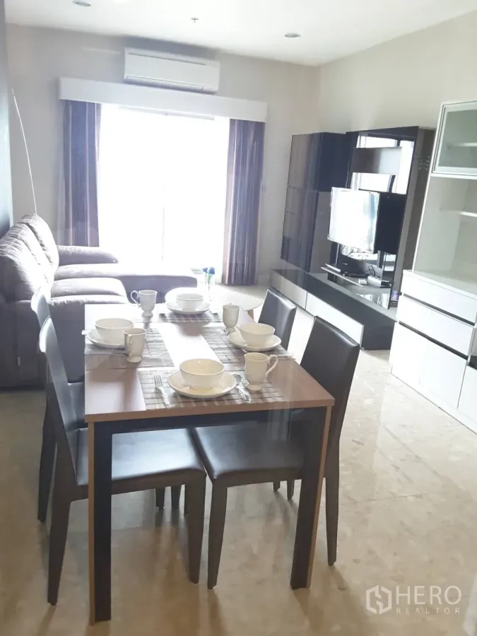 Condominium for rent in Khlong Toei, Bangkok - Open-plan living and dining with an L-shaped sofa, four-seat table, and large window.