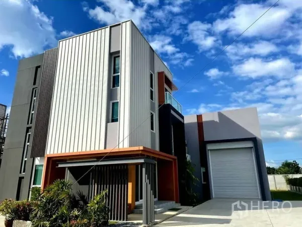 Warehouse for sale in Lam Luk Ka, Pathum Thani - Contemporary home‑office and warehouse facade with roller shutter, landscaped entry and clear blue sky.
