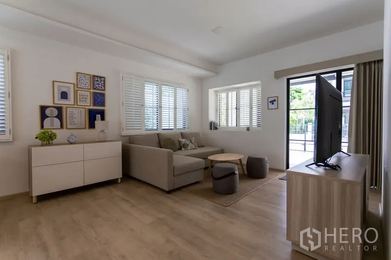 Townhouse for rent in Bang Phli, Samut Prakan - Bright living room with L-shaped sofa, TV console, wood flooring and shuttered windows.