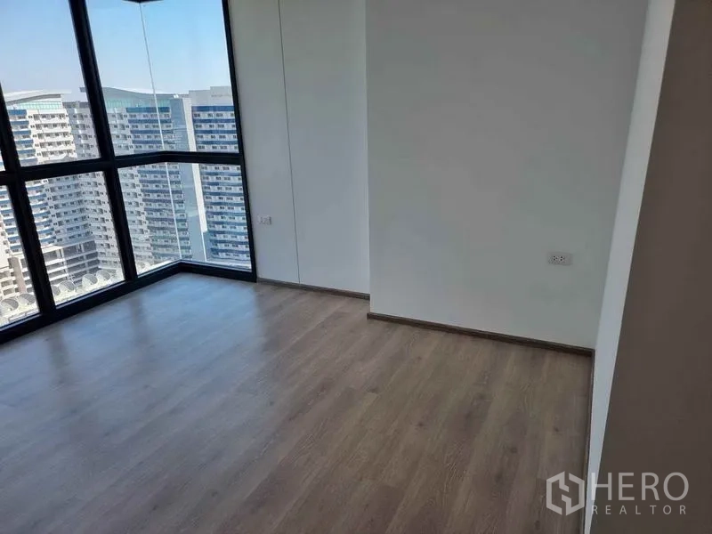 Condominium for sale in Phaya Thai, Bangkok - Empty bedroom with large windows overlooking neighboring towers and the city.