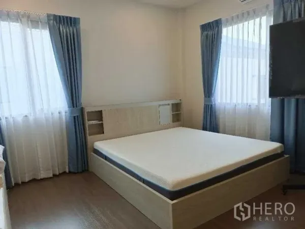 独立式住宅 出租在Mueang Nonthaburi, Nonthaburi - 明亮卧室，落地窗与蓝色窗帘，木地板配大床。
