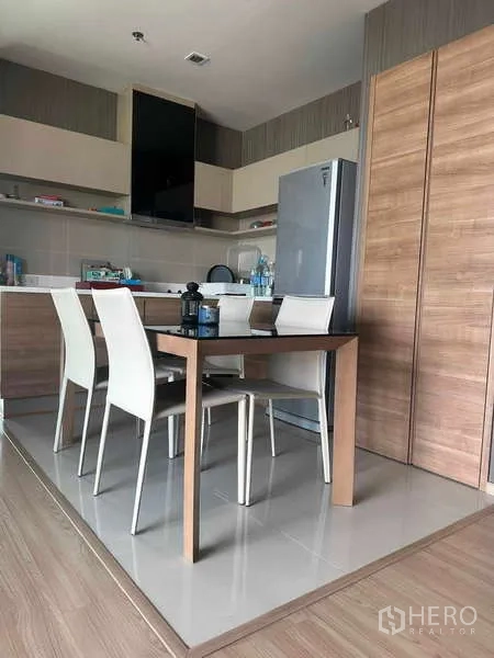 Condominium for sale in Phaya Thai, Bangkok - Close view of dining table beside a modern kitchen with fridge and cabinets.