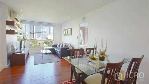 Condominium for rent or sale in Watthana, Bangkok - Open-plan living and dining area with wood floors and large window city views.