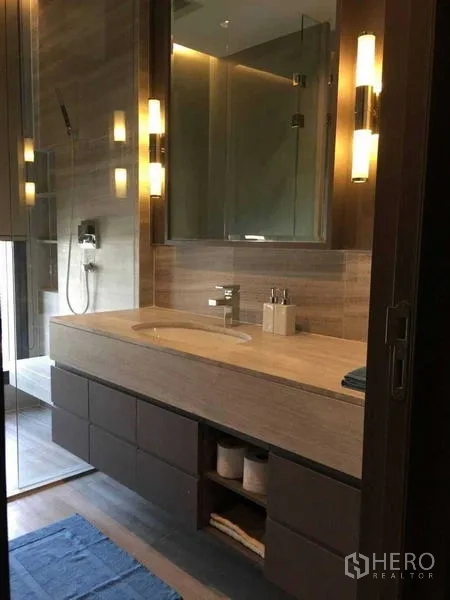 Condominium for rent in Bang Rak, Bangkok - Second view of the bathroom showing long vanity, glass shower, and ambient sconces.