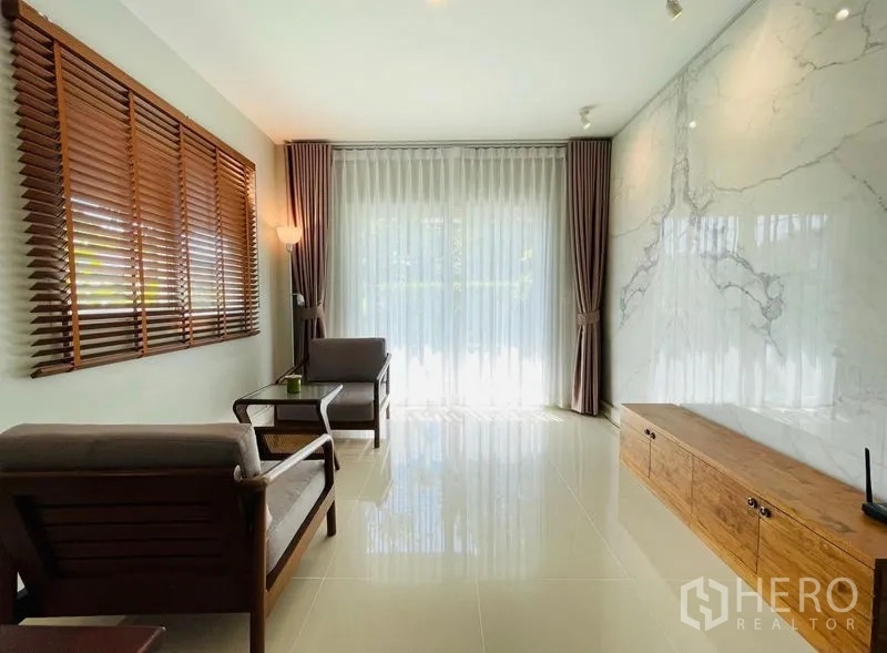 Detached House for sale in Lam Luk Ka, Pathum Thani - Bright sitting area with marble accent wall, floor-to-ceiling curtains and wooden blinds.