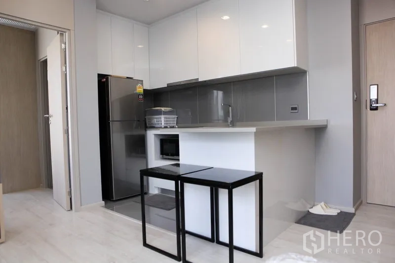 Condominium for rent in Watthana, Bangkok - Sleek white kitchen with glossy cabinets, full-size fridge and peninsula counter.