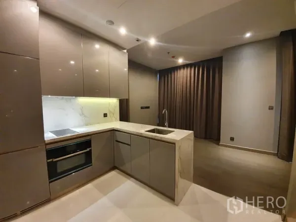 คอนโด ให้เช่าในHuai Khwang, Bangkok - ครัวรูปตัวแอลสไตล์โมเดิร์น เคาน์เตอร์หินอ่อน ตู้บิลต์อิน เตาและเตาอบ พร้อมอ่างล้างจาน ข้างพื้นที่นั่งเล่นมีผ้าม่านทึบ