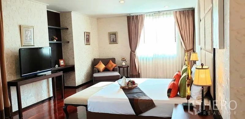 อพาร์ทเมนท์ ให้เช่าในWatthana, Bangkok - ห้องนอนมาสเตอร์กว้าง ไฟแสงนุ่ม ทีวี และเก้าอี้นั่งริมหน้าต่าง