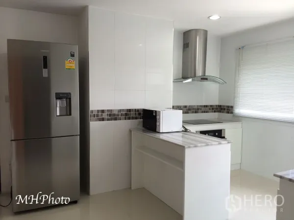 Condominium for rent in Watthana, Bangkok - Bright white kitchen with island, electric cooktop, range hood, mosaic backsplash and stainless-steel refrigerator.