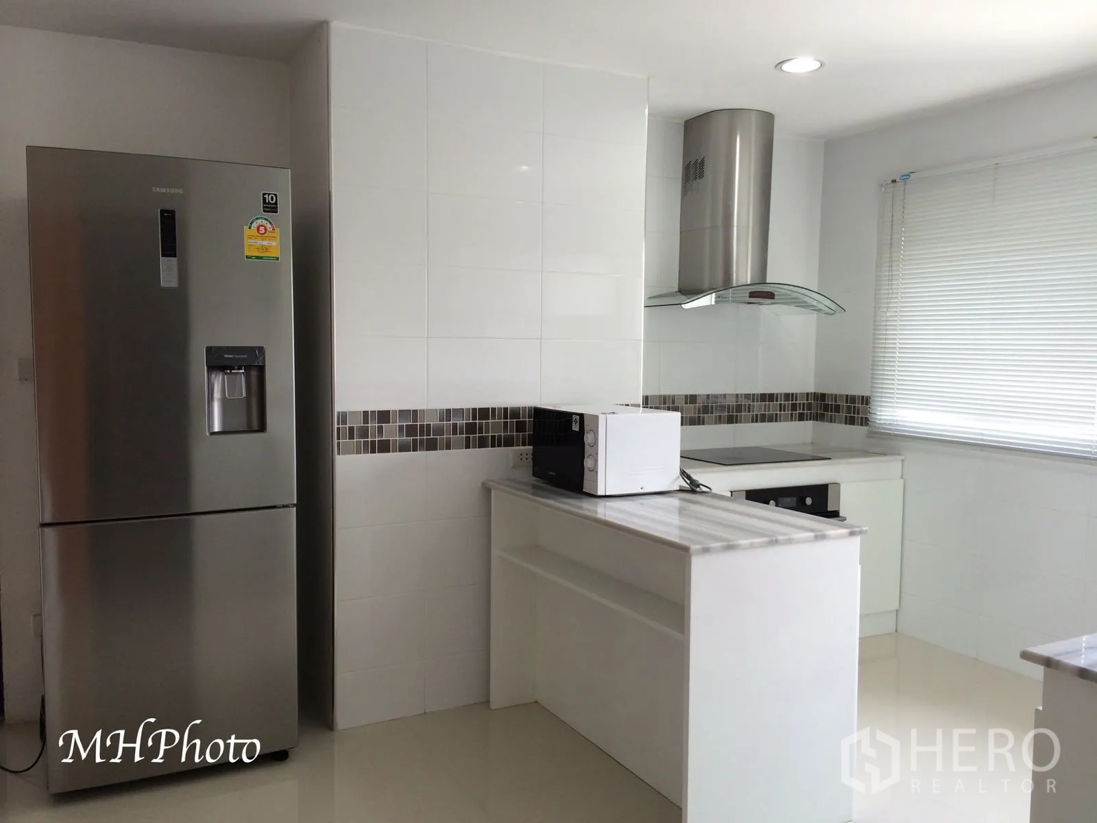 Condominium for rent in Watthana, Bangkok - Bright white kitchen with island, electric cooktop, range hood, mosaic backsplash and stainless-steel refrigerator.