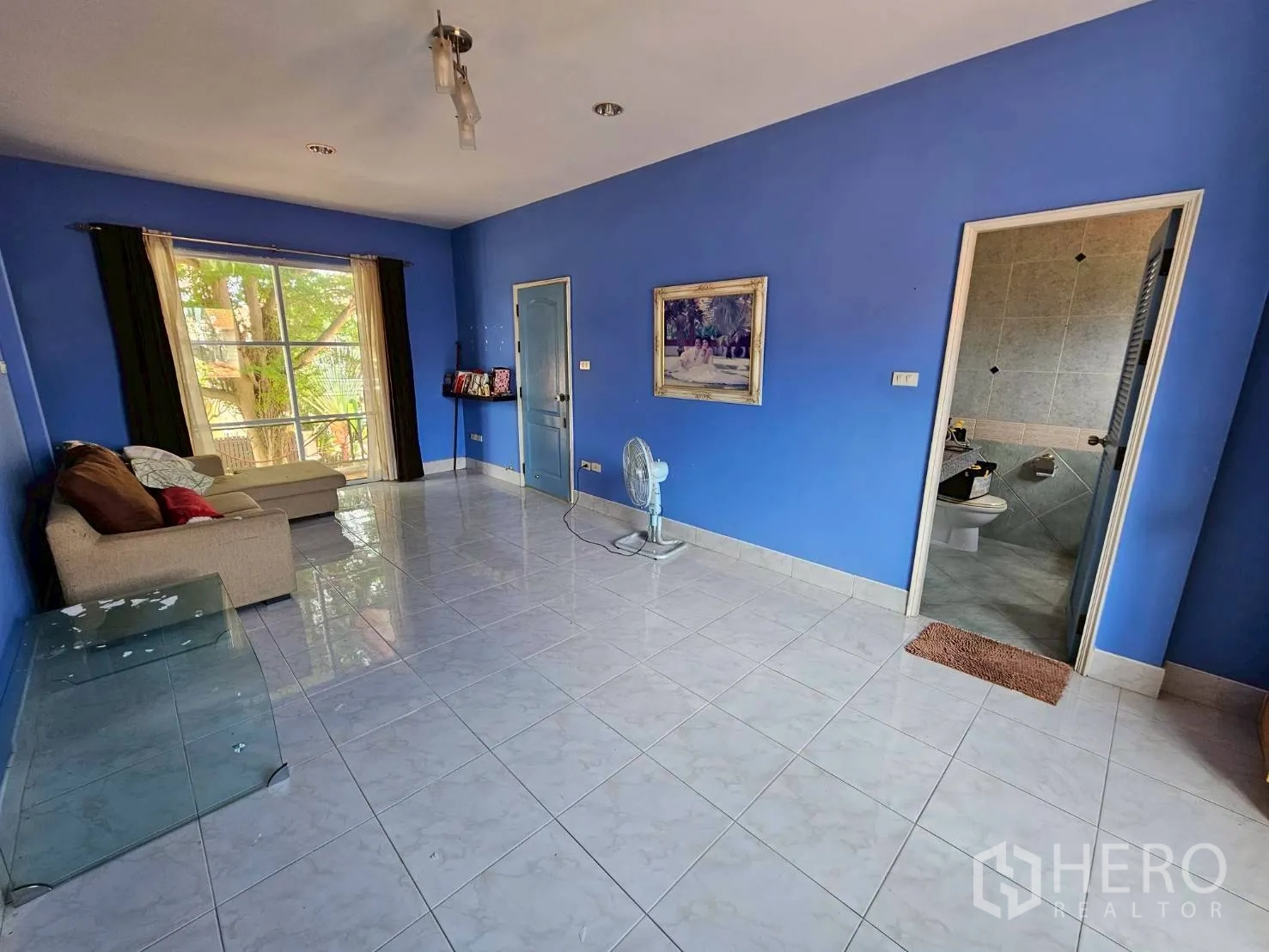Detached House for rent or sale in Bang Lamung, Chon Buri - Spacious blue primary bedroom with sofa, balcony window, and ensuite.